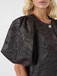 Juoda tekstūruota palaidinė su didelėmis pūstomis rankovėmis, išmantriu klostavimu ir dekoratyviniu metaliniu mygtuku prie kaklo.