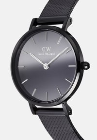 Montre analogique noire avec un cadran dégradé gris, des index en argent et un bracelet en caoutchouc avec un motif texturé.