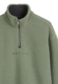 Bluza polarowa w stonowanym zielonym kolorze, z kołnierzem na zamek błyskawiczny i wyhaftowanym logo. Materiał o fakturze, miękki, z lekko miękką powierzchnią.