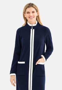 Navy fleece long jacket with white accents, zip closure, high collar, and two front pockets. Soft texture and casual design.