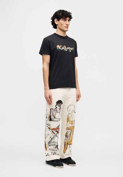 Μαύρο βαμβακερό t-shirt με πολύχρωμο γραφικό κείμενο, συνδυασμένο με εκρού παντελόνια που διαθέτουν καλλιτεχνικά σχέδια καθιστών φιγούρων και λεπτομέρεια υπογραφής.