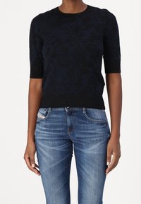 Mörkblå blommönstrad stickad tröja med korta ärmar och ribbad kant, ihop med ljusblå denimjeans.