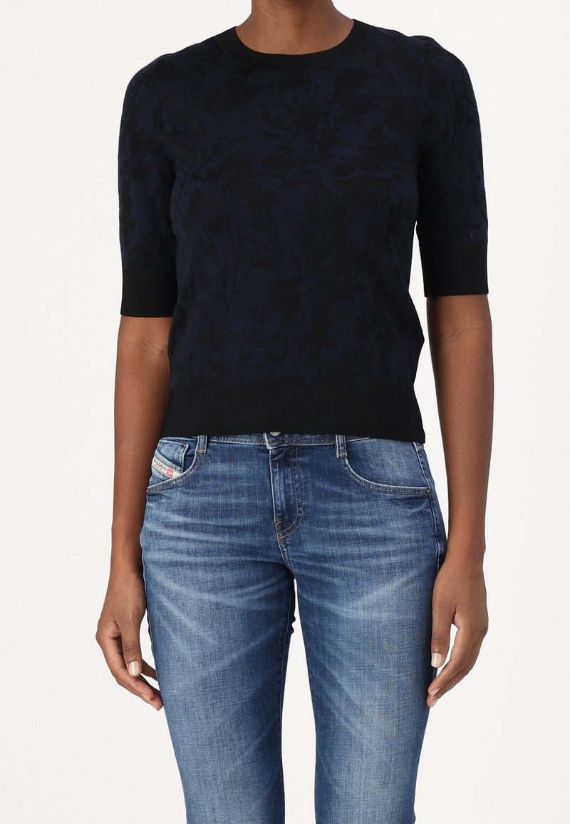 Mörkblå blommönstrad stickad tröja med korta ärmar och ribbad kant, ihop med ljusblå denimjeans.