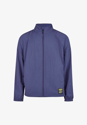 Purple zipper jacket with high collar, lightweight fabric, elastic cuffs, and a distinctive logo patch on the left side.