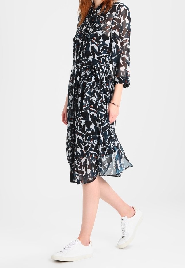 Robe noire avec motif abstrait blanc et bleu, longueur mi-mollet, tissu léger, taille cintrée, associée à des baskets blanches.