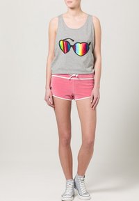 Débardeur gris avec un graphique de lunettes de soleil arc-en-ciel, associé à un short rose avec cordon de serrage et bord blanc. Porté avec des baskets claires.