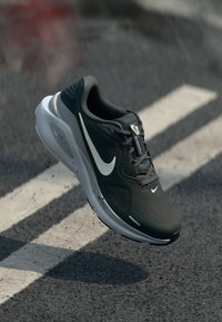 Schwarzer Sportschuh mit einem Obermaterial aus Mesh, reflektierenden Akzenten, gepolsterter Zunge und weißem Swoosh-Logo. Gepolsterte Sohle für Komfort und Unterstützung.