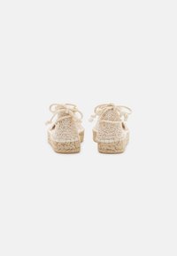 Sandali espadrille intrecciati beige con superficie strutturata, dotati di lacci e suola rialzata. Ideali per un look casual.