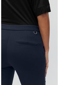 Dunkelblaue Hose mit glatter Textur, ausgestattet mit einer eleganten Gesäßtasche und einer dekorativen Metallschlaufe am Bund.