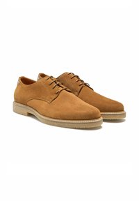Chaussures en suede marron à lacets avec un bout rond, un dessus texturé et une semelle en caoutchouc de couleur claire. Présente un petit logo sur le talon.