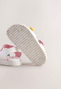 Weiße Sandalen mit rosa, grünen und gelben Akzenten. Strukturierte, gemusterte, flexible Sohlen. Glattes Obermaterial mit Ausschnitt-Designs.
