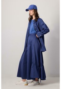 Blauwe katoenen shirt, bijpassend t-shirt en hooggesneden rok met plooien; gecombineerd met witte sneakers en een blauwe pet. Gladde textuur, relaxte pasvorm.