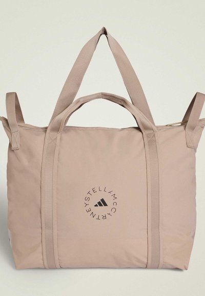 Beige tote bag lavet af stof med to hænder. Har et cirkulært logo i sort og en lynlås lukning i toppen.
