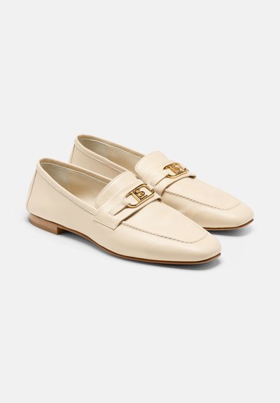 Mocassins en cuir crème avec un design de mocassin, présentant une astuce de boucle en or et un petit talon en bois. Texture lisse et détails cousus.
