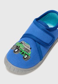 Zili kanvas slide ar velcro siksnu. Uz pirksta ir zaļa un pelēka izšūta monstru kravas mašīna. Pelēks gumijas zole ar ribām.