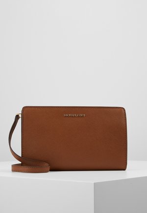 Brown textured leather wristlet clutch with gold Michael Kors logo and matching leather strap resting on white surface.