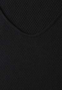 Gros plan d’un tissu noir montrant deux textures tricotées avec une couture courbe séparant un motif alvéolé d’une surface tricotée lisse.
