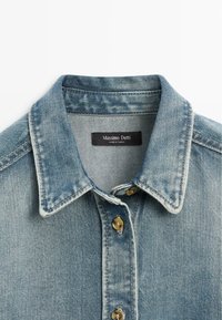 Světle modrá džínová košile s špičatým límcem a hnědými knoflíky, označeno Massimo Dutti, vyrobeno v Tunisku.