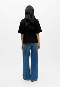 T-shirt en coton noir à coupe décontractée, associé à un jean large bleu clair avec poches arrière et une simple finition ourlée.