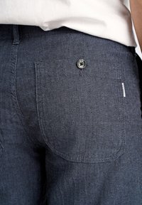 Dunkelblå herringbone-mönstrad tyg, med en bakficka med en svart knapp; mjuk textur med subtila linjer.