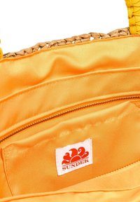 Borsa di stoffa gialla con manici in tessuto intrecciato. L'interno presenta una fodera arancione liscia e una piccola tasca con zip. Include un'etichetta con logo bianco.