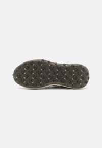La suola della scarpa sportiva presenta una superficie in gomma nera texturizzata con piccole impugnature circolari, delimitata da un bordo beige a contrasto.