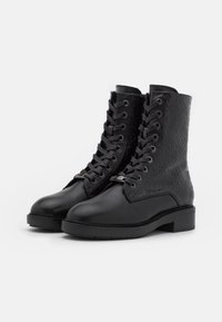 Black lace-up combat boots with a textured, embossed logo pattern, rounded toe, and a low block heel. Made of smooth leather.