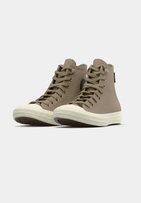High-top canvas sneakers in light brown with round toe, white rubber sole, and classic lace-up design. Features logo on the side.