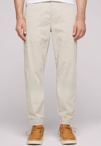 Pantalons cargo beige effilés avec poches latérales et détails cousus, associés à des chaussures en daim marron à lacets.