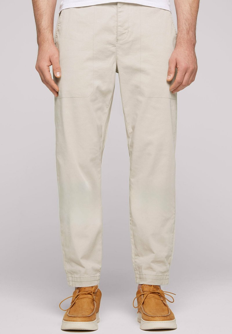 Pantalons cargo beige effilés avec poches latérales et détails cousus, associés à des chaussures en daim marron à lacets.