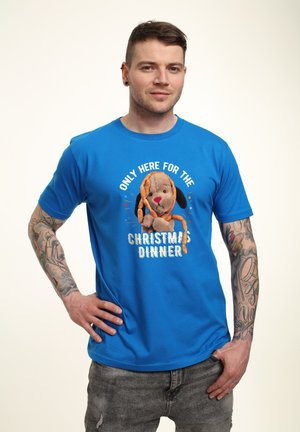 Blå bomulds T-shirt med et grafisk motiv af en brun hund og teksten "KUN HER FOR JULEMIDDAG" i hvid og orange skrift.