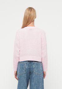 Ροζ πλεκτό πουλόβερ με κοντό σχεδιασμό, ανοιχτή πλέξη υφής και μακριά μανίκια. Φορεμένο με ανοιχτό μπλε τζιν με σχέδια.