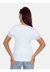 Biała koszulka z krótkim rękawem z koronkowym wykończeniem rękawów, gładka faktura, z okrągłym dekoltem, w zestawie z jasnoniebieskimi dżinsami.