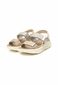 Sandalia de tela beige y plata con correas anchas, cierres ajustables y una suela blanca gruesa con un diseño texturizado.