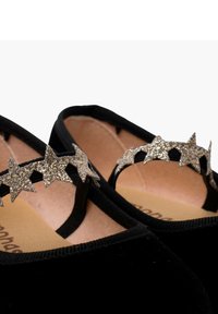 Black velvet shoes featuring a strap adorned with glittery silver star accents. The interior has a neutral beige insole.