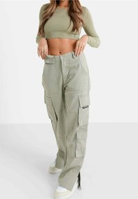 Pantalon cargo vert clair avec de multiples poches, coupe droite et taille haute. Fabriqué à partir d'un tissu durable. Souligné de détails de couture.