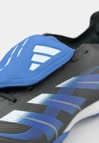 Svart og blå sportssko med teksturert overflate, blå detaljer og hvite stripemønstre, samt en polstret blå pløse og svarte lisser.