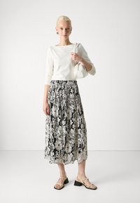 Hvit langermet topp, svart skjørt med hvit blomsterbroderi, beige sandaler med stropper, og en liten hvit håndveske. Glatte teksturer, flytende design.