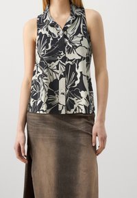 Blouse sans manches à fleurs en noir et crème, avec col à revers, fermeture par boutons et coupe décontractée. Assortie à une jupe marron.