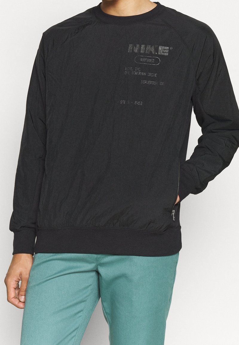 Sweatshirt noir à manches longues avec une finition texturée et un ourlet côtelé contrastant. Présente des éléments de marque imprimés et des détails dans une finition mate subtile.