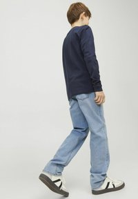 Camisa de manga larga de color navy combinada con unos vaqueros de mezclilla azul claro y zapatillas blancas con detalles en negro. Ajuste casual y relajado apropiado para un uso diario.