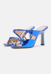 Plave metalik sandale s potpeticom, s ukrštenim trakama i otvorenim prstima. Potpetica je tanka sa četvrtastim bazom za stabilnost.