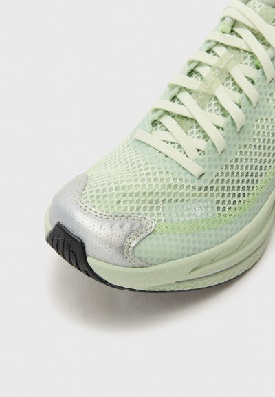 Hellgrüner Laufschuh mit Mesh-Obermaterial, reflektierender silberner Zehenkappe, strukturiertem schwarzen Sohlen und flachen Schnürsenkeln. Besitzt eine numerische Detailangabe an der Seite.