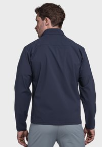 Marineblauer Softshell-Jacke mit einem strukturierten Kragen, langen Ärmeln und einer glatten, wasserabweisenden Textur. Besitzt ein tailliertes Design und diskrete Nähte.