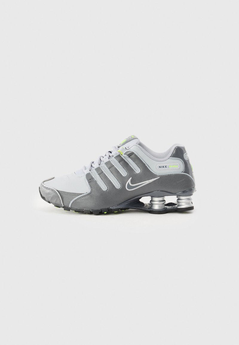 Damnarski čevlji Nike Shox vključujejo mešanico sivo-belih materialov, s strukturno zgornjim delom, oblazinjenim ovratnikom in značilnim zasnovo pete na vzmet.