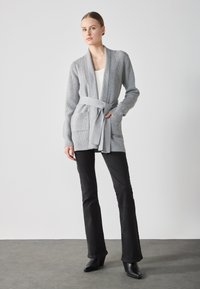 Grå ribbad cardigan med bred krage, en knytbälte i midjan och två framfickor, tillsammans med svarta utsvängda byxor och klackboots.