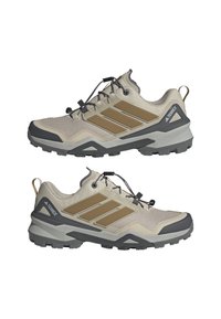 Scarpe da trekking beige caratterizzate da una tomaia in mesh testurizzato, dettagli grigi, un design con tre strisce marroni e una suola in gomma rugged con chiusura a lacci.