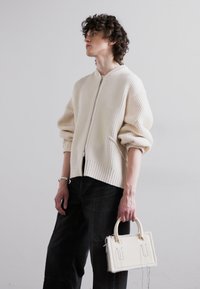 Cream ribbed bomber jacket with a zip front, worn over black loose-fit pants, holding a small white structured handbag.
