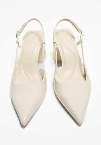 Talons slingback en cuir verni beige avec un bout pointu, un petit talon carré et une fine bride au niveau de la cheville. Texture lisse avec une finition brillante.