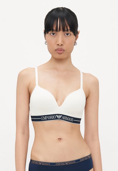 White plunge bra with adjustable straps, featuring a navy elastic band with "EMPORIO ARMANI" logo. Smooth texture, minimalist design.